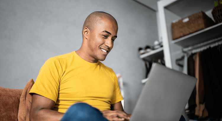Man sitting on couch looking at laptop computer and smiling