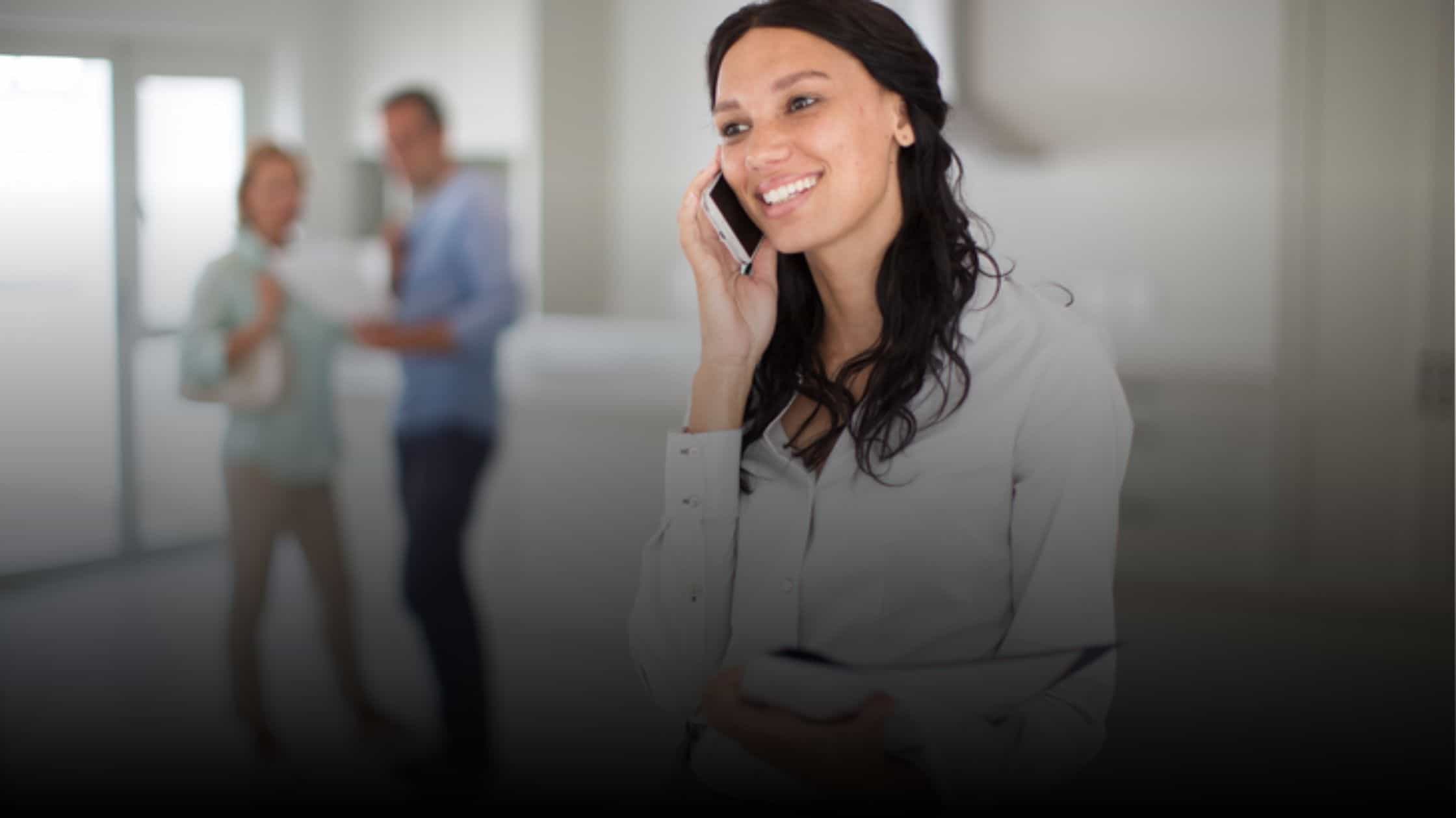 Real estate agent on the phone with her home buyers standing behind her