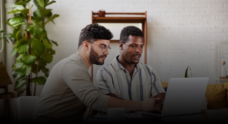 Two men sitting at a table looking at a laptop computer