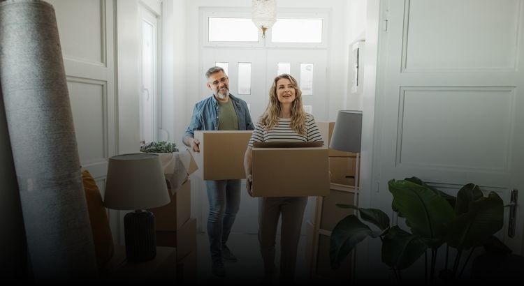 Photo of a man and woman carrying moving boxes into a home