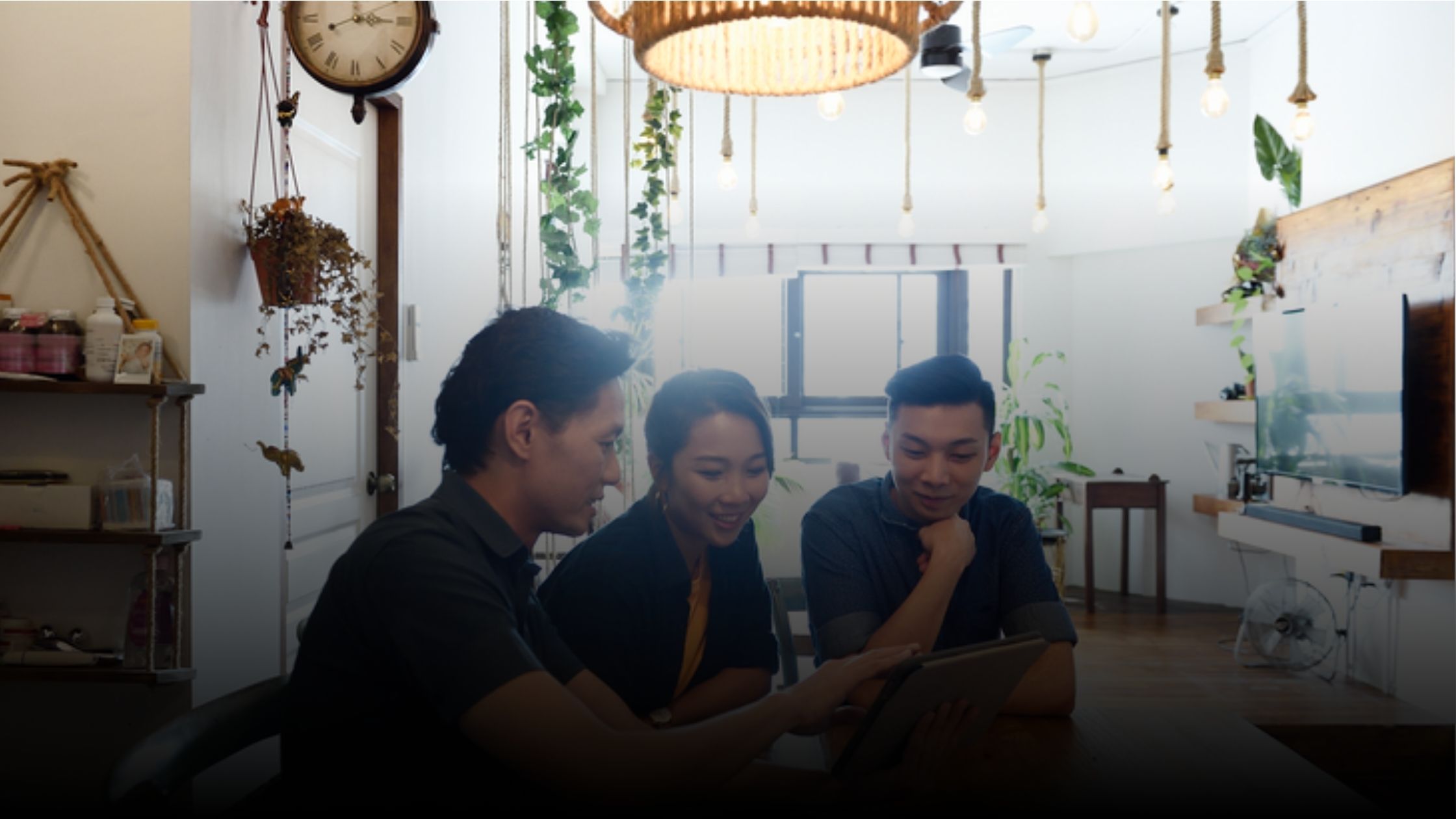 Three people gathered around a table looking at a tablet computer