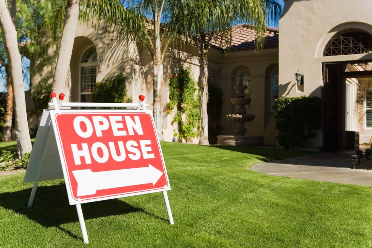 Red open house directional sign with arrow on green lawn in front of a luxury home in the Fox Valley Tri-Cities IL area